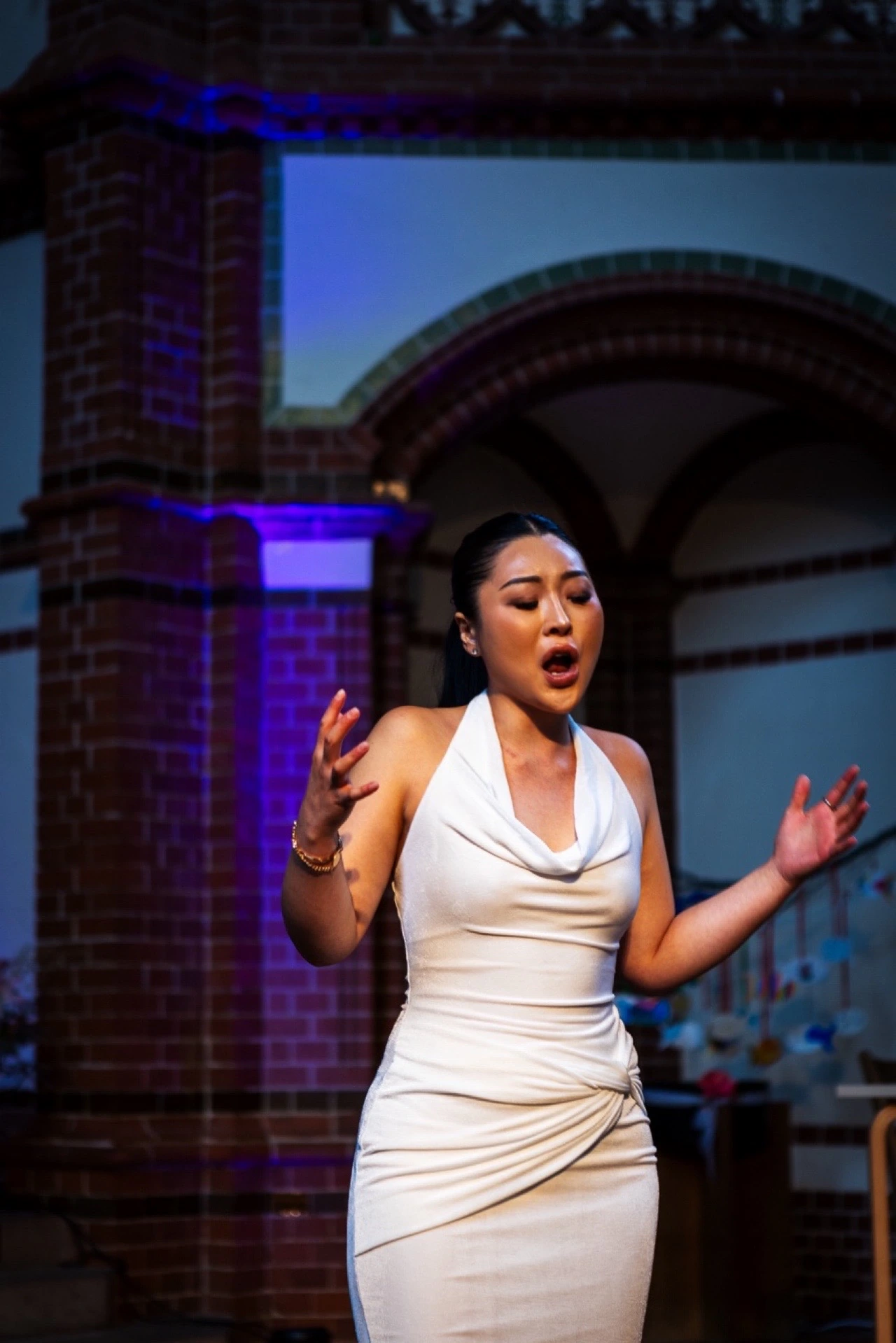 Daoun Jung singing on stage in a white gown under violet light